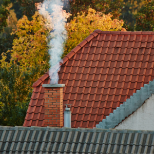 smoking chimney with a red-roofed house in the background and a tree with yellow leaves