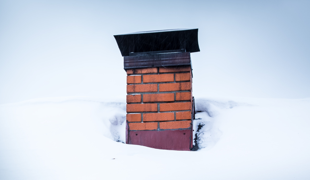 a brick chimney surrounded by a snowy roof