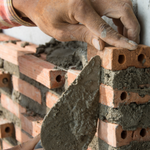 a hand placing a brick on a wall with brick and mortar