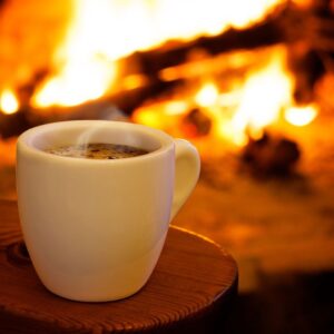 a cup of steaming coffee in front of a blazing fireplace