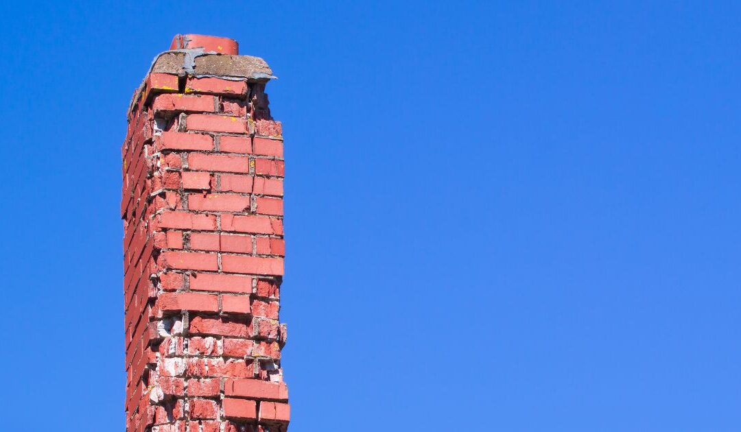 a red brick chimney with lots of damage and missing brick and mortar against a blue sky